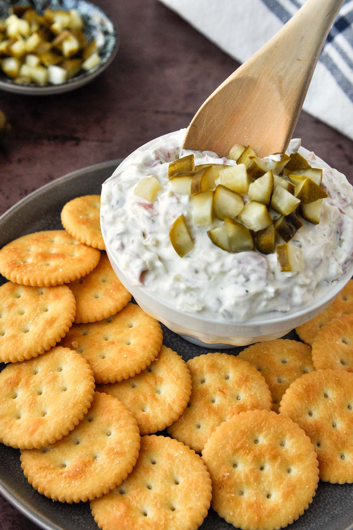 A bowl of pickle wrap dip with a wooden spoon on a tray of crackers.