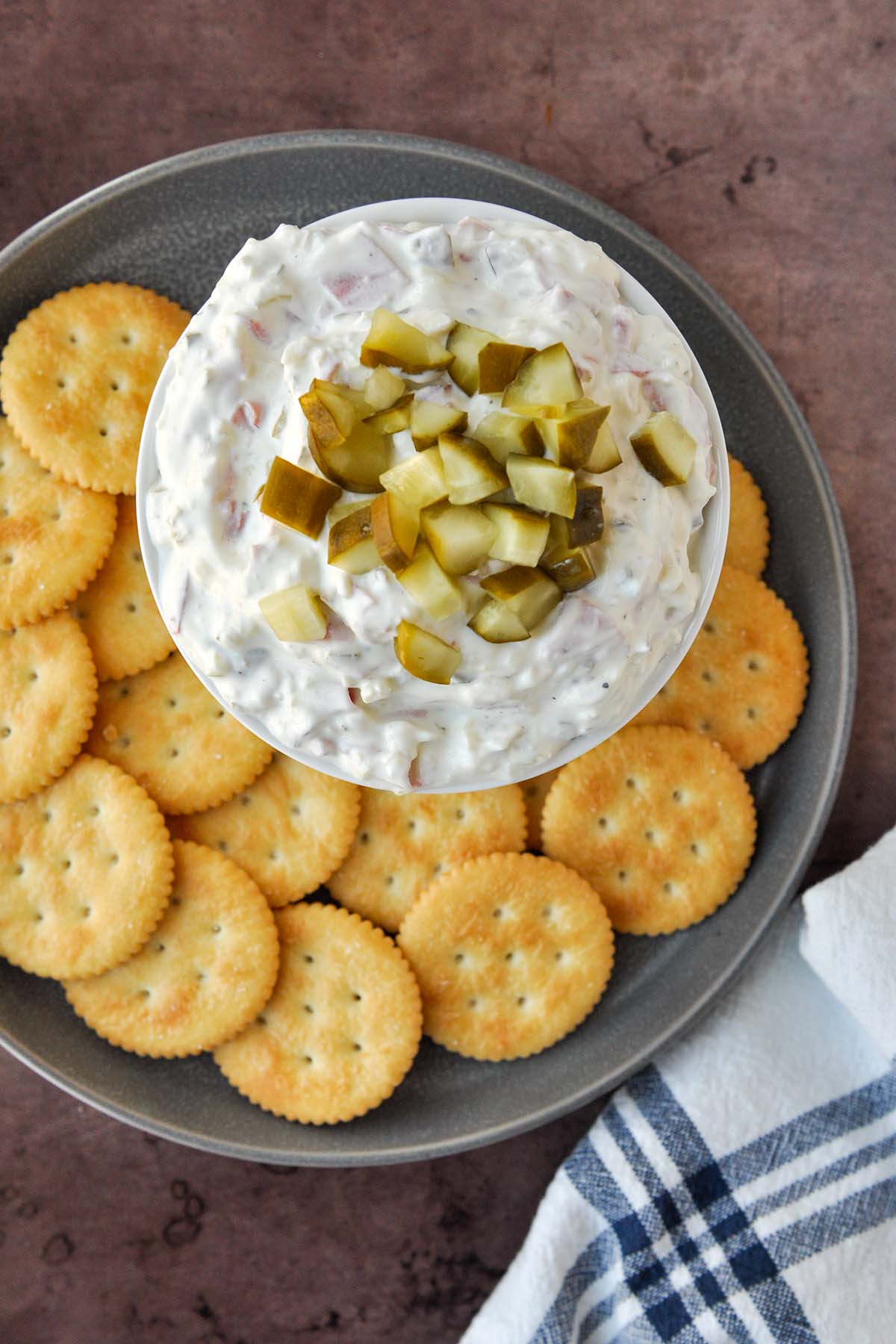 Above view of a bowl of pickle wrap dip on a tray of crackers with a blue and white towel.