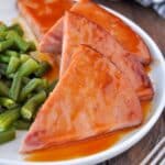A plate of triangles of ham slices drizzled with sauce, with a side of green beans.