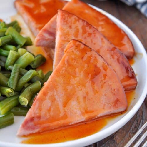 A plate of triangles of ham slices drizzled with sauce, with a side of green beans.