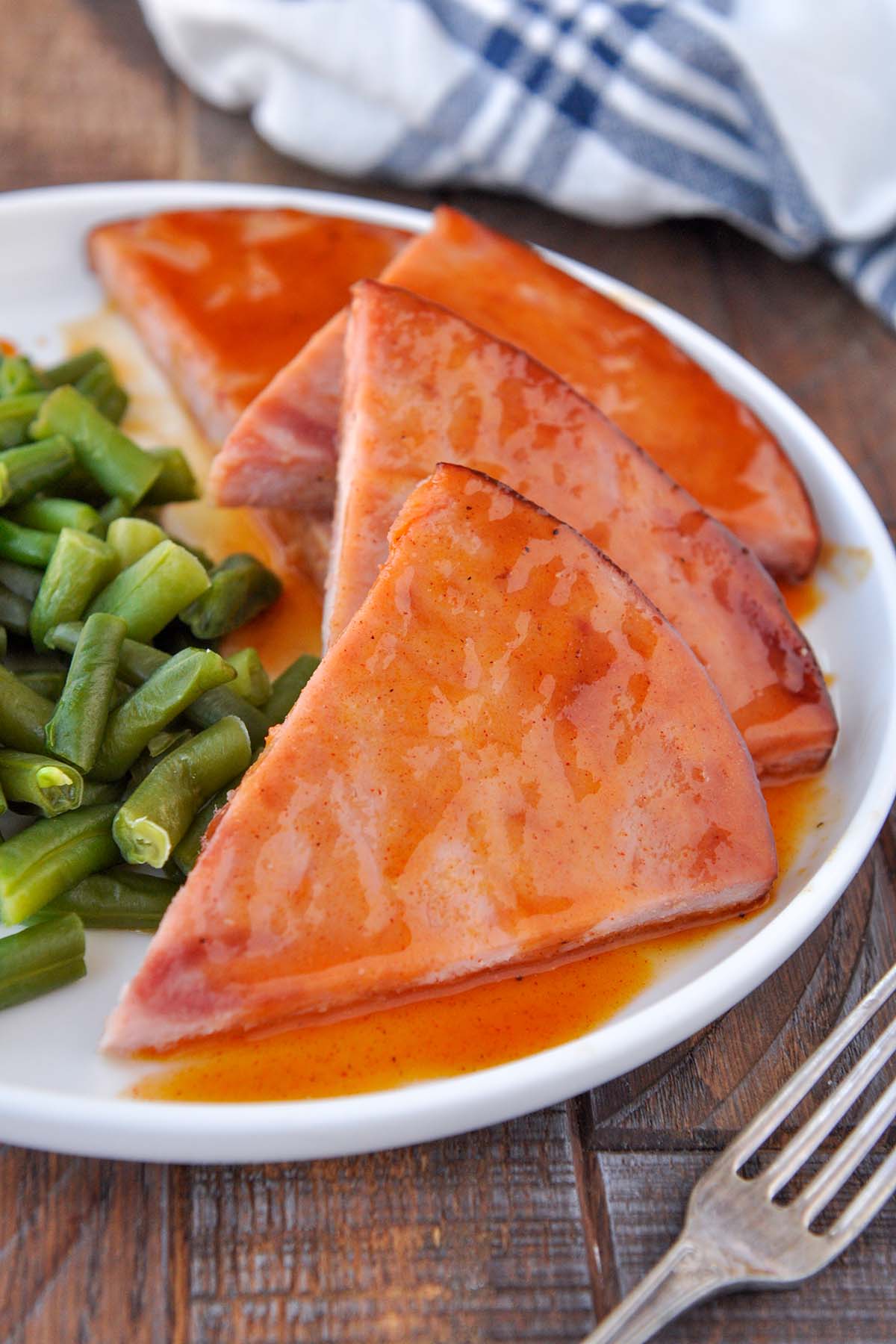A plate of triangles of ham slices drizzled with sauce, with a side of green beans.