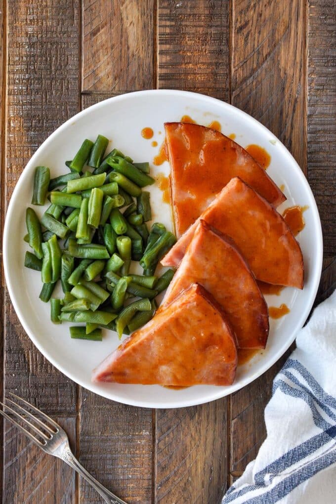 Above view of a plate of ham slices drizzled with sauce, with a side of green beans.