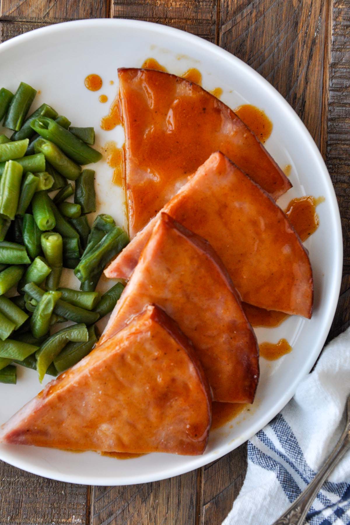 Above view of a plate of triangles of ham slices drizzled with sauce, with a side of green beans.