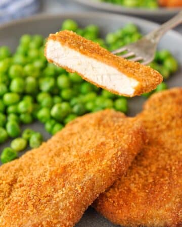 A bite of pork chop on a fork over a plate of pork chops and peas.