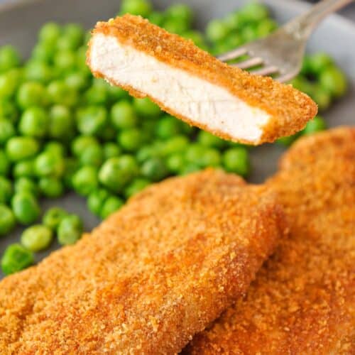 A bite of pork chop on a fork over a plate of pork chops and peas.