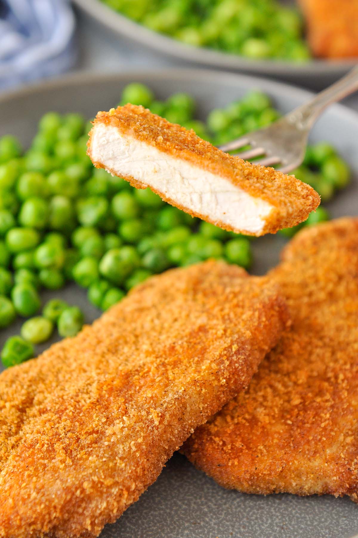 A bite of pork chop on a fork over a plate of pork chops and peas.