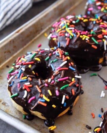 Up close of a baking sheet of cooked and chocolate glazed donuts with sprinkles.
