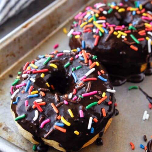 Up close of a baking sheet of cooked and chocolate glazed donuts with sprinkles.