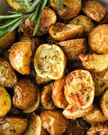 Above view of a baking dish of air fried potatoes with a striped towel, garlic bulb, and a sprig of fresh rosemary.