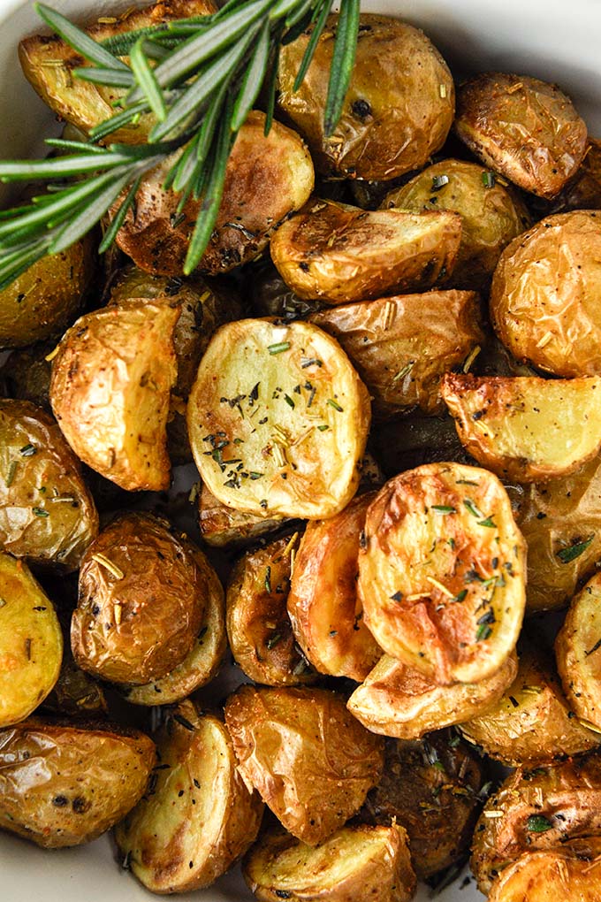 Above view of a baking dish of air fried potatoes with a striped towel, garlic bulb, and a sprig of fresh rosemary.