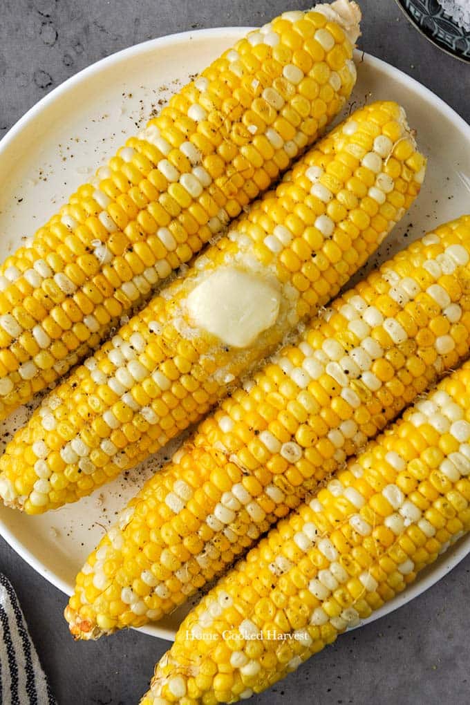 A plate of four cooked corn cobs with a pat of melty butter.