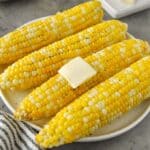 A plate of four cooked corn cobs with a pat of melty butter.