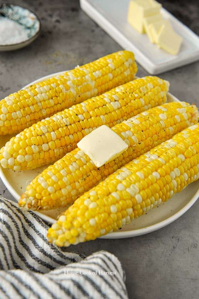 A plate of buttered corn on the cob with a striped towel and a plate of butter.