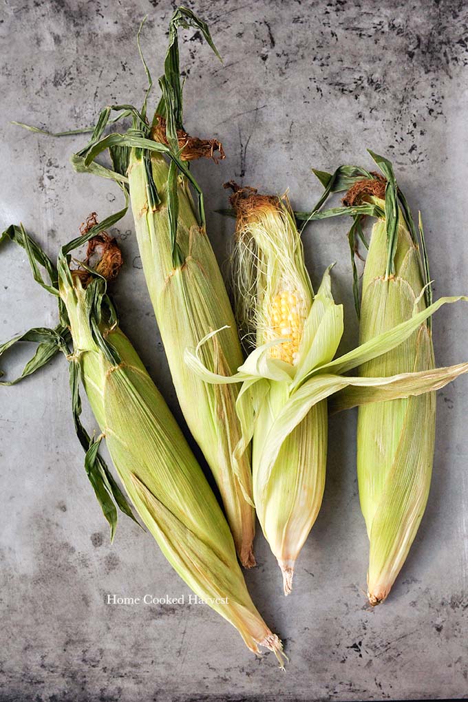 The ingredients needed to make air fryer corn on the cob. Four ears of corn that are needing to be shucked.