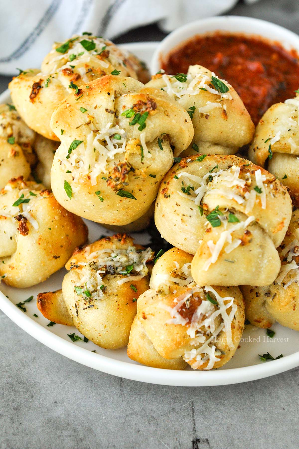 A plate full of garlic knots with a small bowl of marinara sauce.