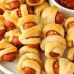 A plate of baked mini mummy's with a bowl of ketchup.