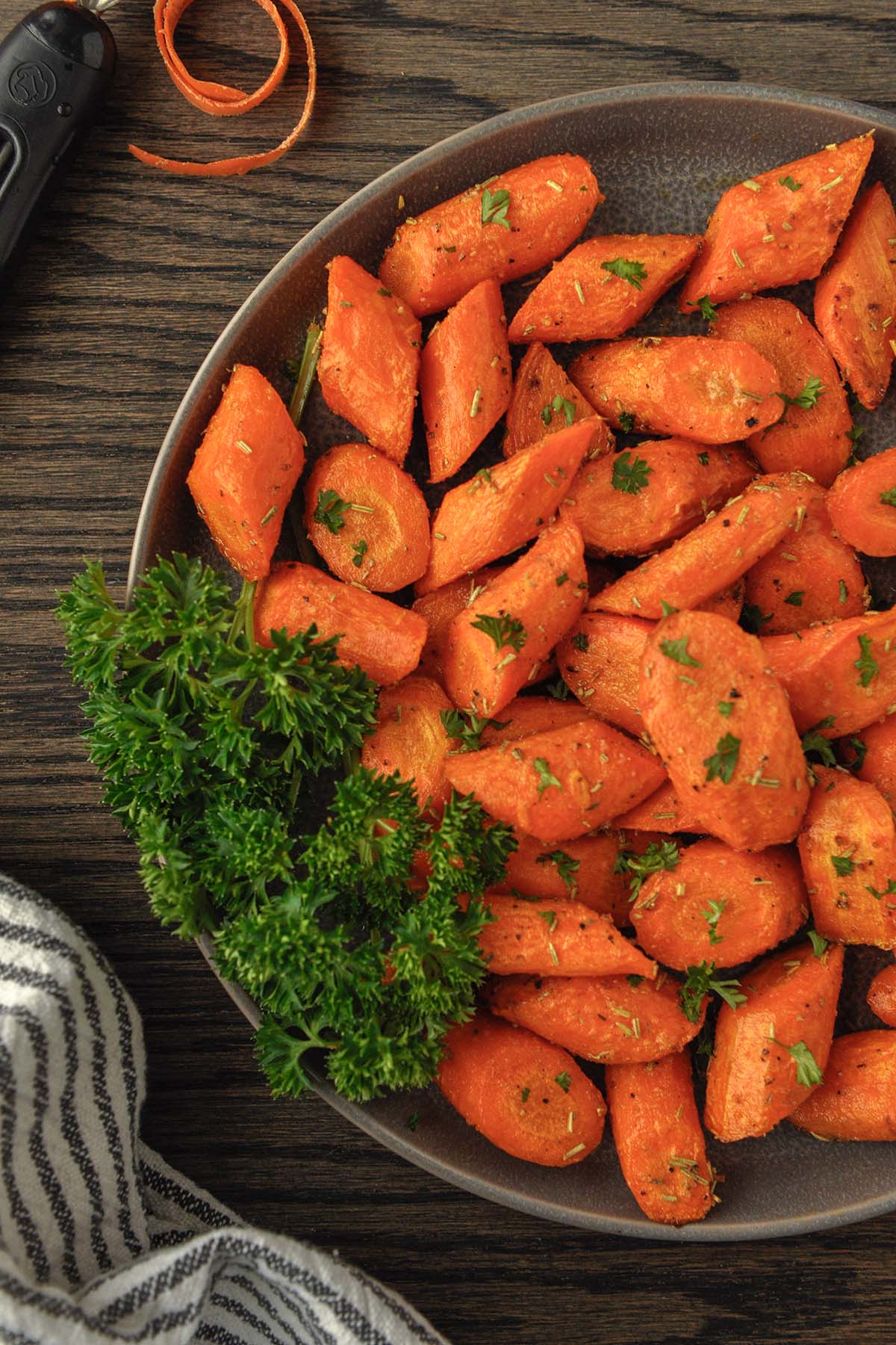 Above view of a plate of air fried carrots with some parsley and a striped towel.