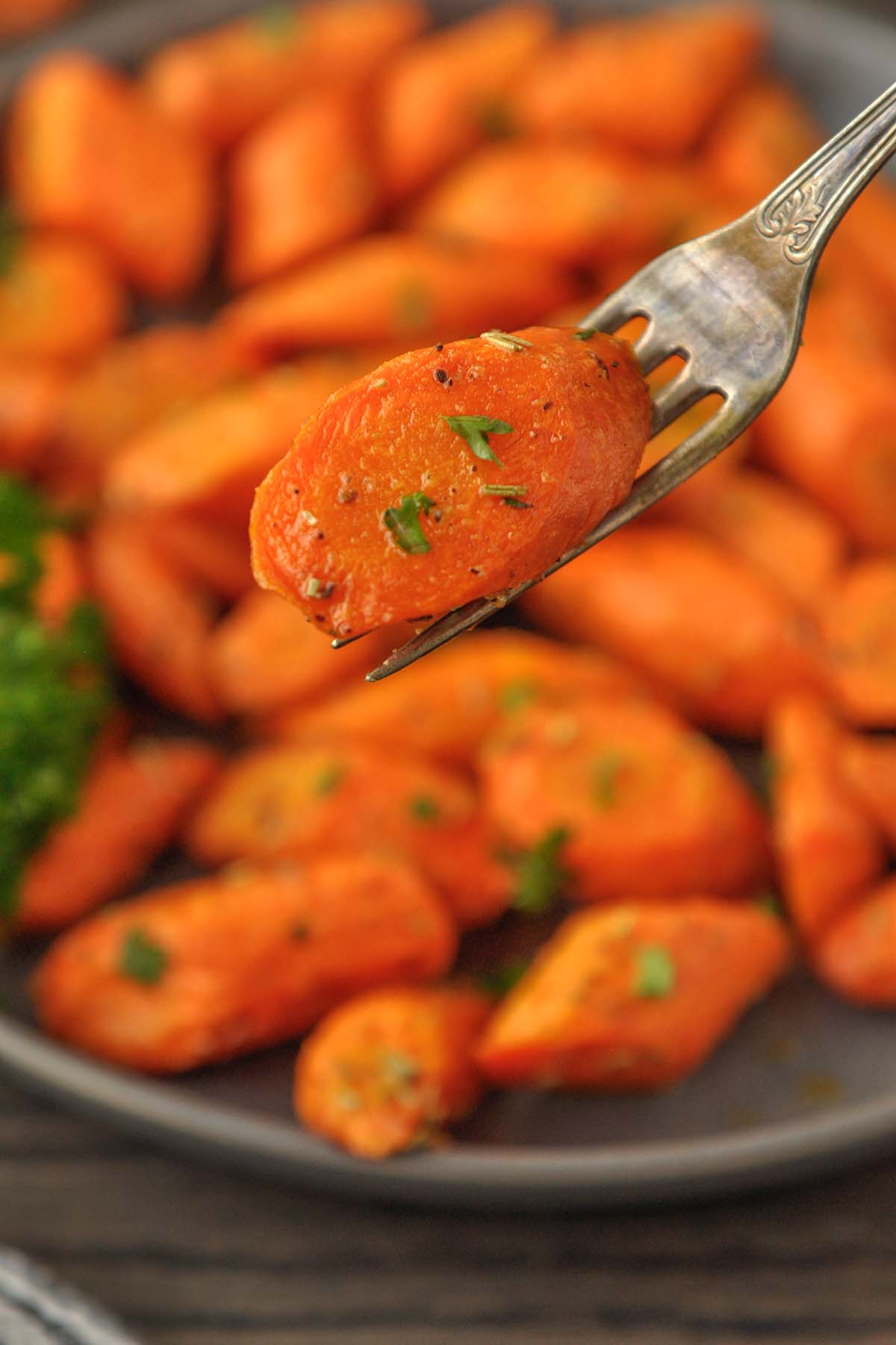 Up close of a carrot on a fork over a plate of carrots.