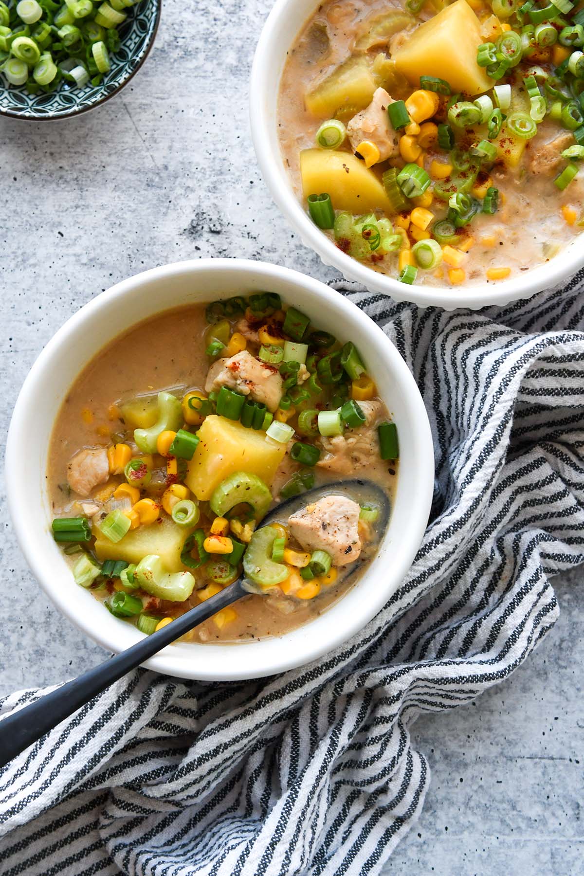 Above view of two bowls of chicken corn chowder with a striped towel  and a small bowl of green onions.