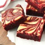 Cheesecake swirled brownies on a wooden tray with a red and white striped towel in the background.