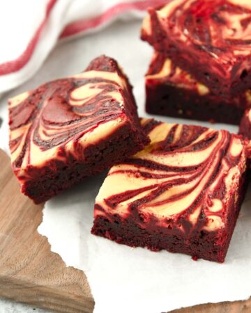 Cheesecake swirled brownies on a wooden tray with a red and white striped towel in the background.