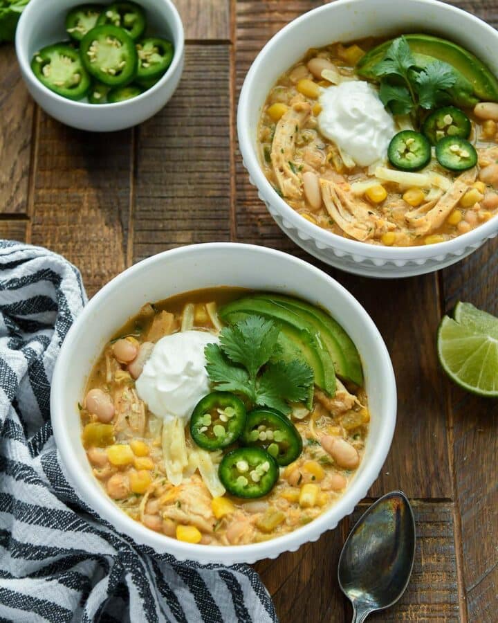 Above view of two bowls of chicken chili with some lime slices and a bowl of jalapeno slices.