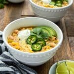 Two bowls of chicken chili with some lime slices and a bowl of jalapeno slices.