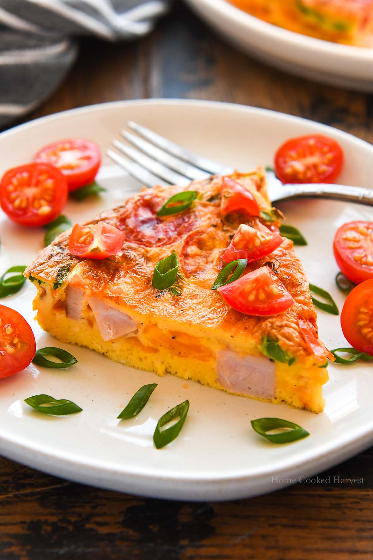 Up close of a slice of frittata on a plate sprinkled with cut tomatoes and green onions.