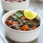 Two bowls of chili with a tray of chips and a striped towel. Topped with lime slices and cilantro.