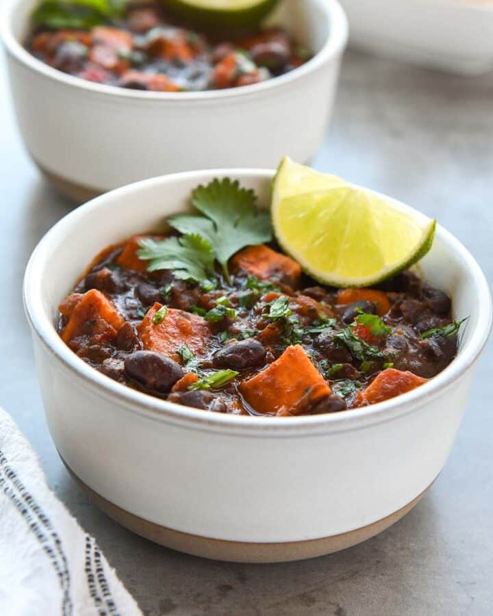 Two bowls of chili with a tray of chips and a striped towel. Topped with lime slices and cilantro.