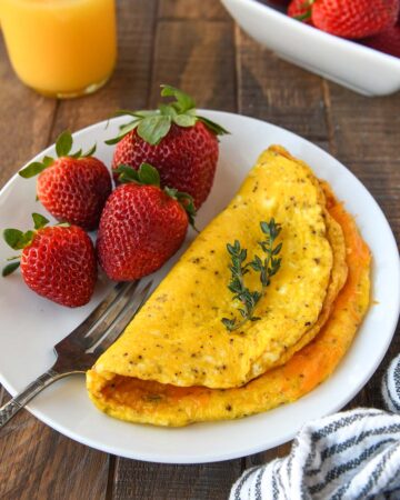 A fluffy omelet on a white plate with fresh strawberries and a glass of orange juice.