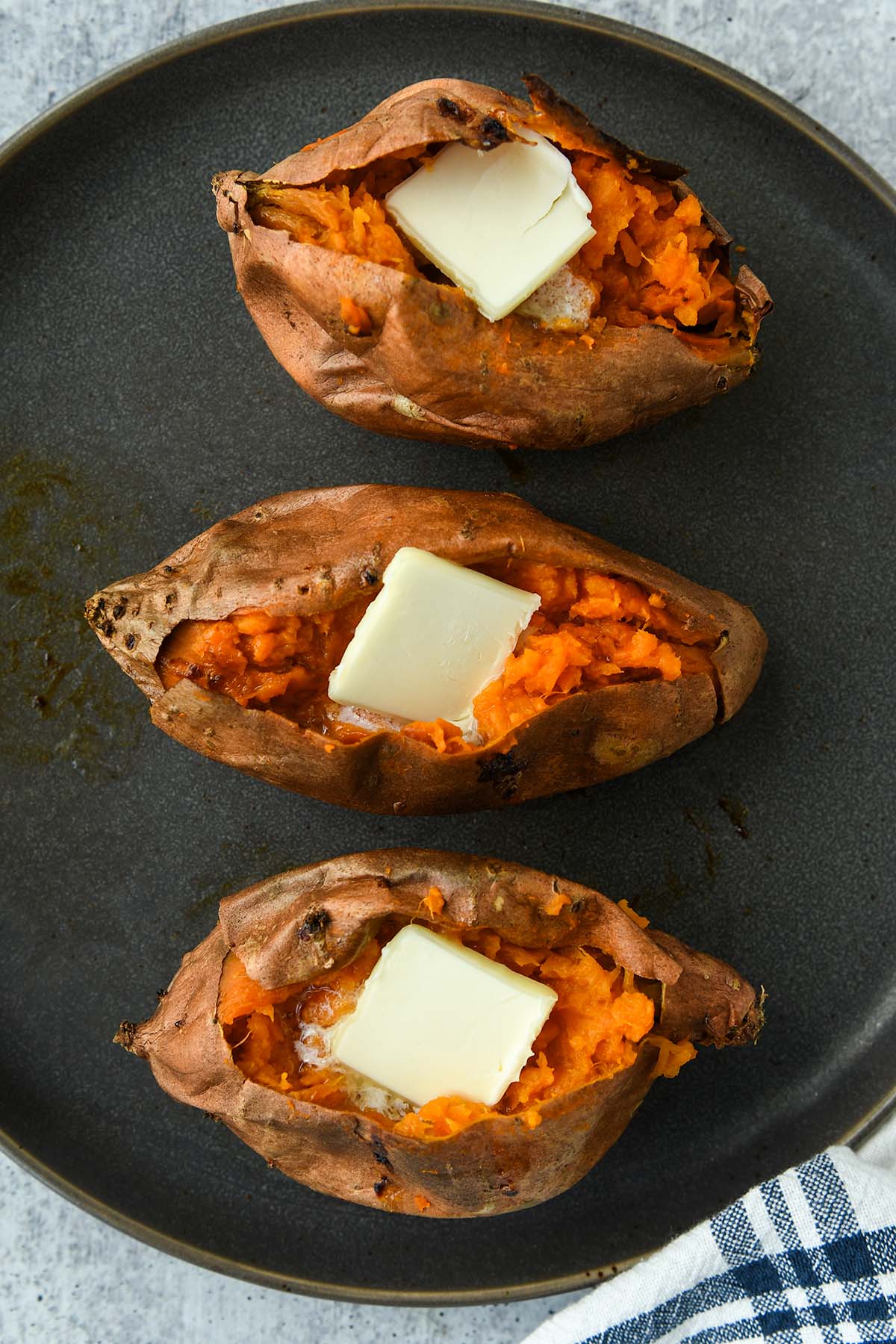 Above view of three sweet potatoes all topped with butter.