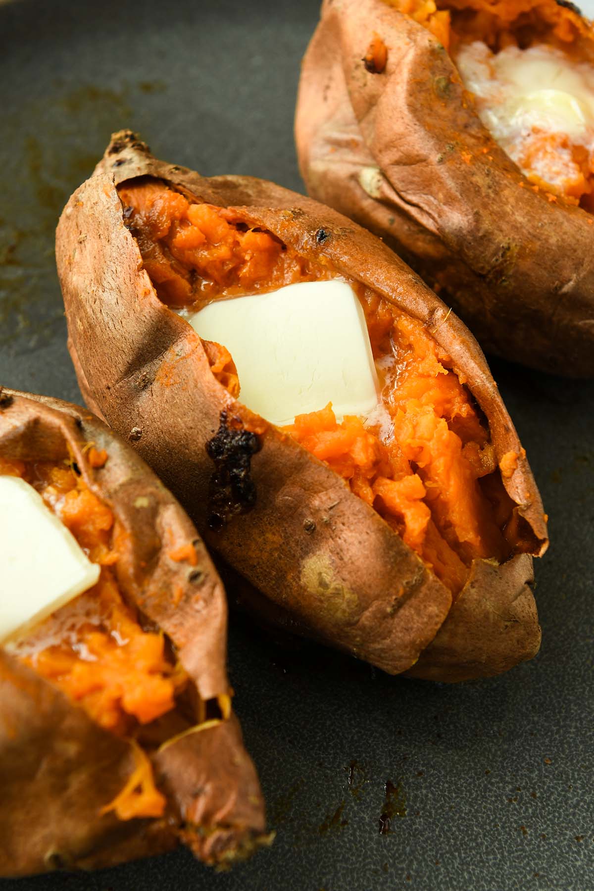 Above view of three cooked sweet potatoes topped with butter.