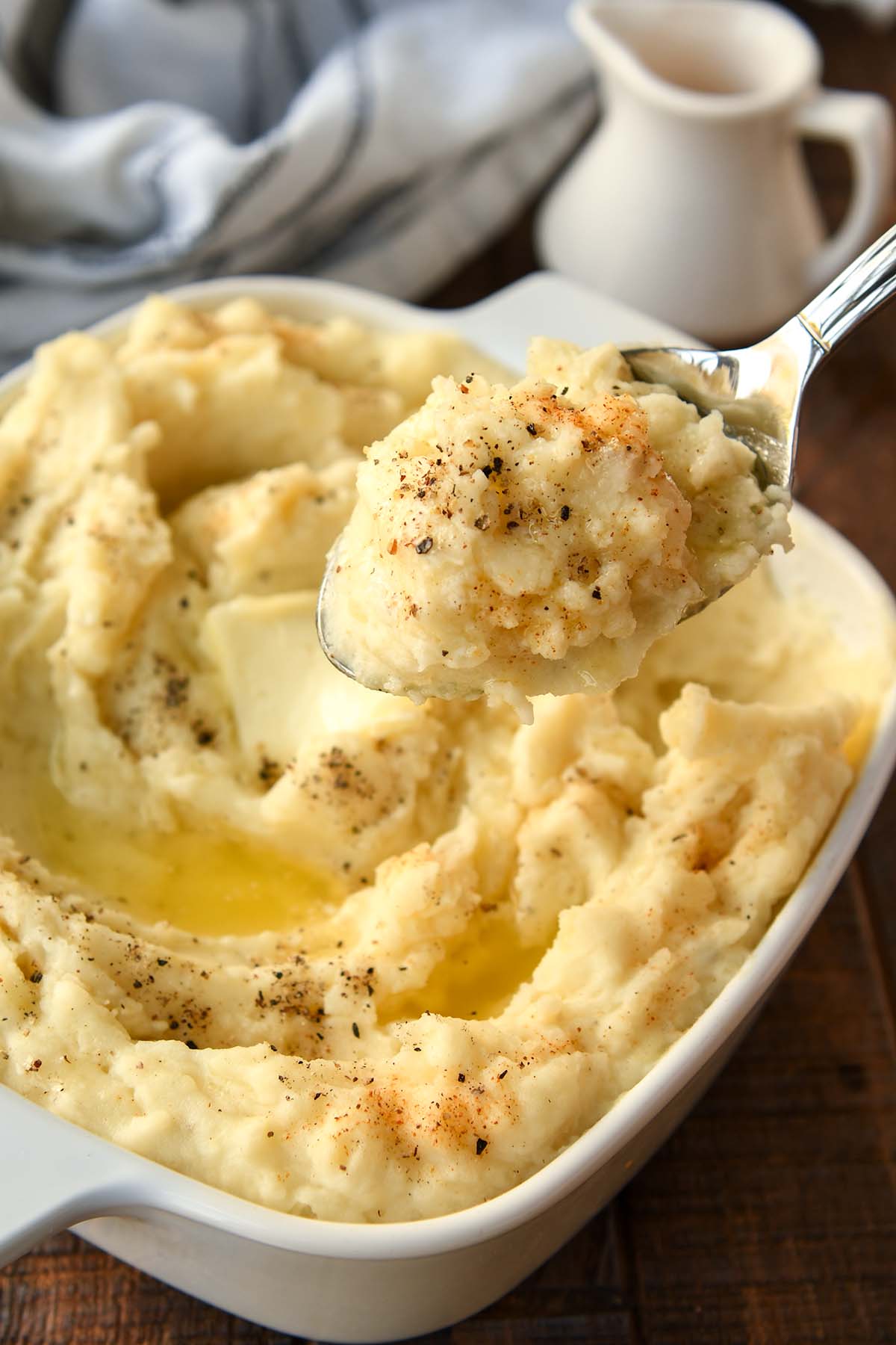 A big spoonful of mashed potatoes over a big dish of buttery, peppered potatoes.