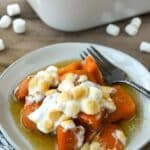 A plateful candied yams with a fork and a baking dish and marshmallows around.