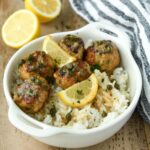 A white bowl of meatballs over rice with some lemon slices and a striped towel.