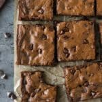Above view of cut up brownies on brown parchment with a cutting knife and some chocolate chips