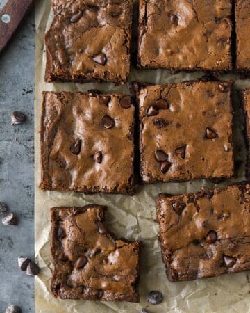 Above view of cut up brownies on brown parchment with a cutting knife and some chocolate chips