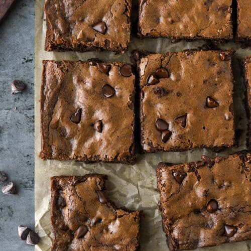 Above view of cut up brownies on brown parchment with a cutting knife and some chocolate chips