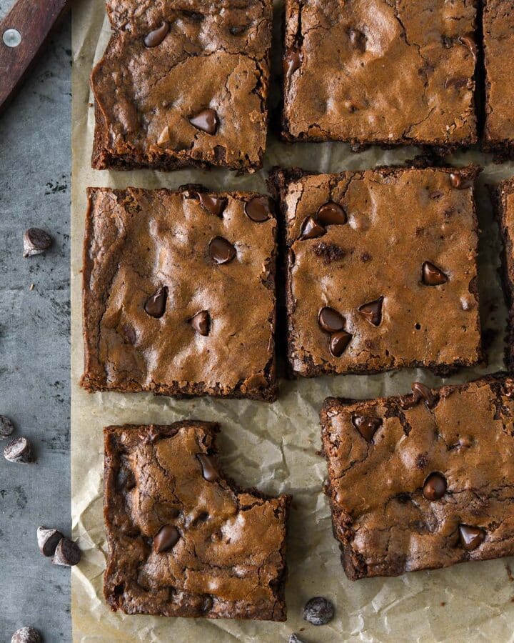 Above view of cut up brownies on brown parchment with a cutting knife and some chocolate chips