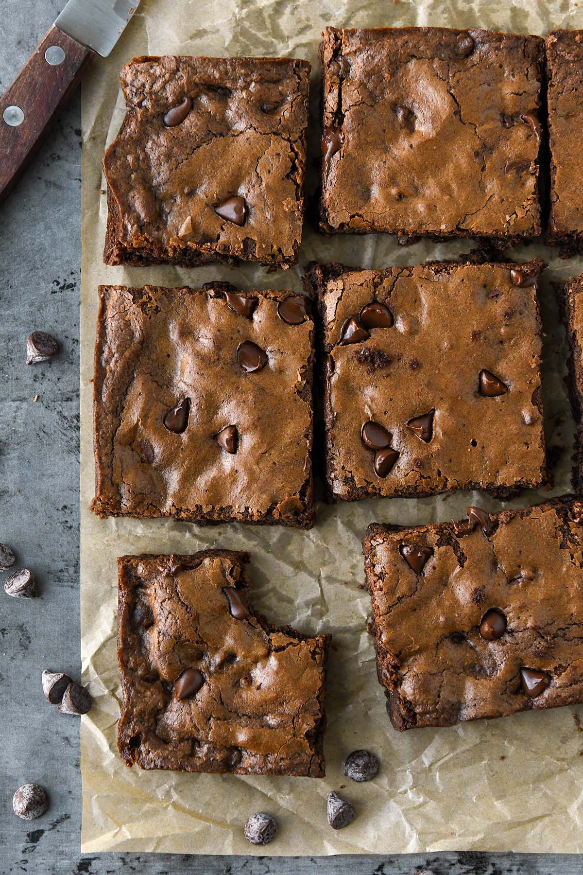 Above view of cut up brownies on brown parchment with a cutting knife and some chocolate chips