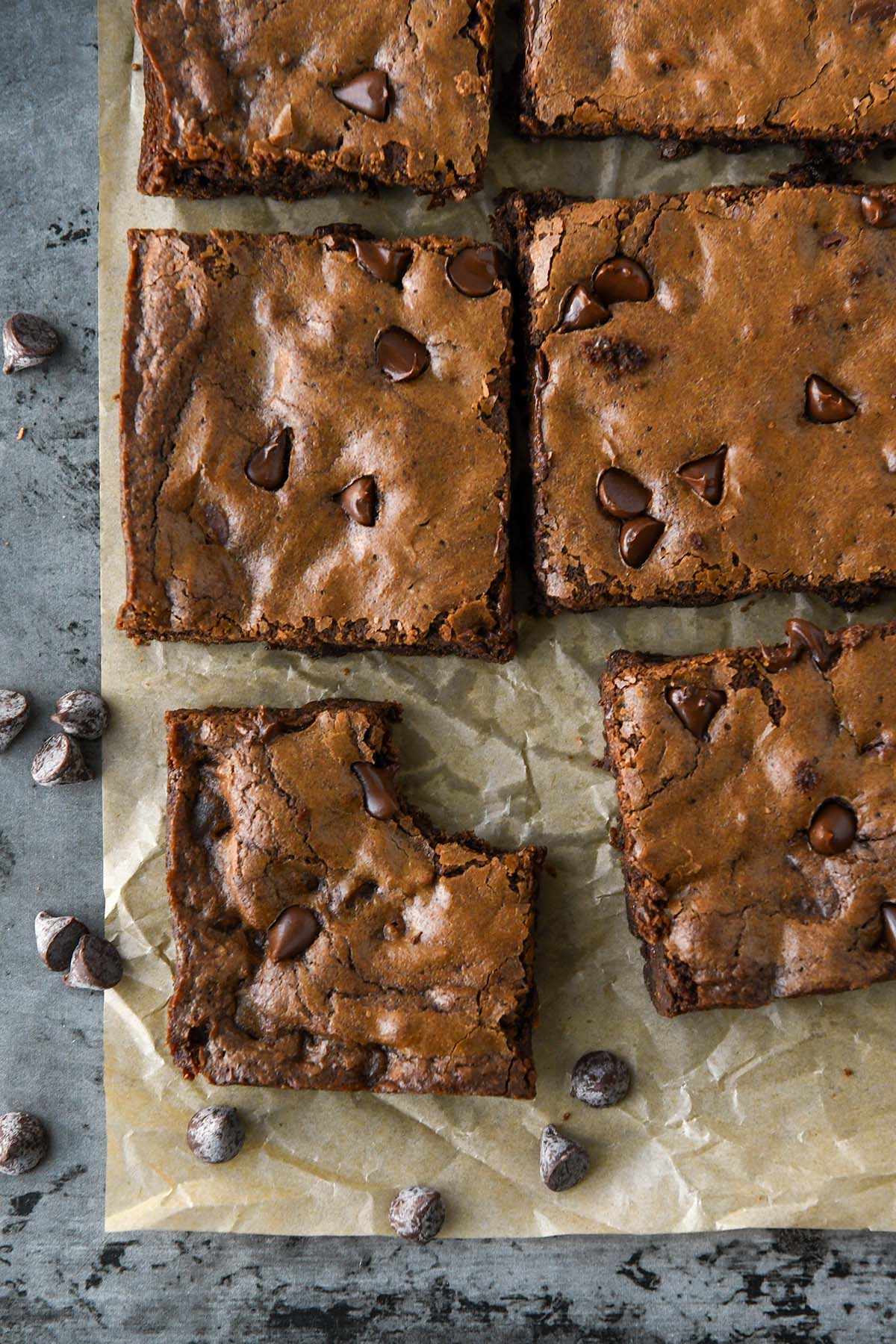 Above view of cut up brownies on brown parchment with some chocolate chips.
