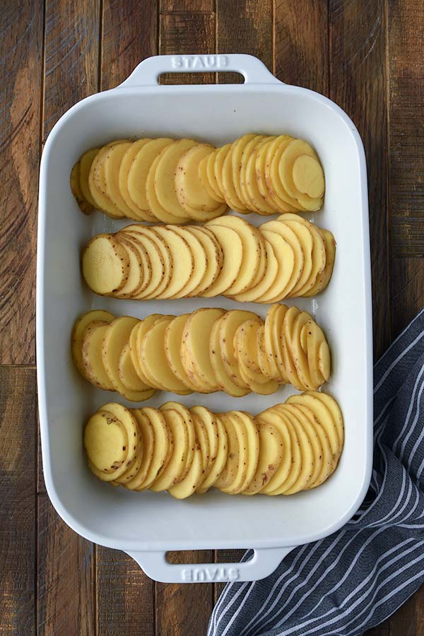 Step one is all of the sliced potatoes lined up in a white baking dish.