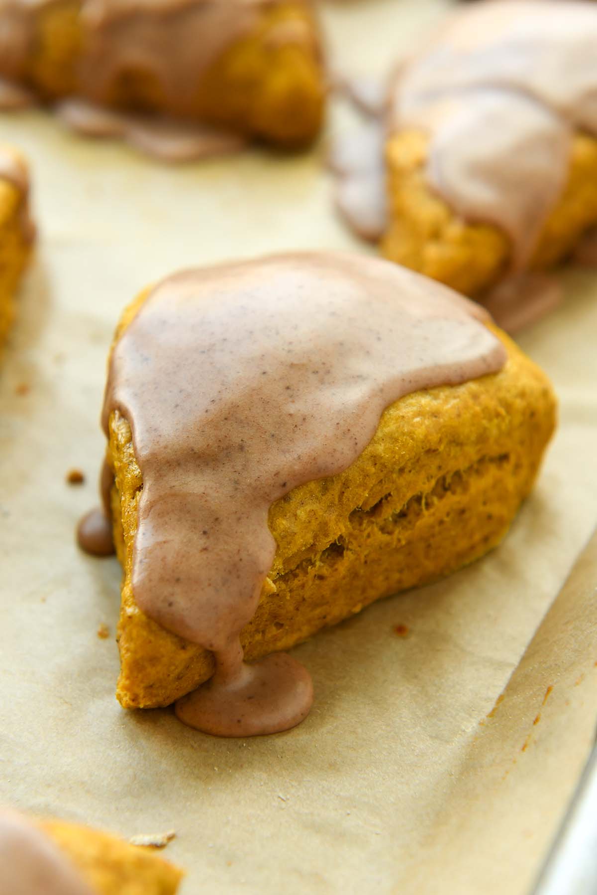 Up close of a pumpkin scone with icing on a baking sheet.
