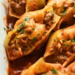 Up close of a stuffed shell sprinkled with chopped cilantro surrounded my other shells in a white baking dish.