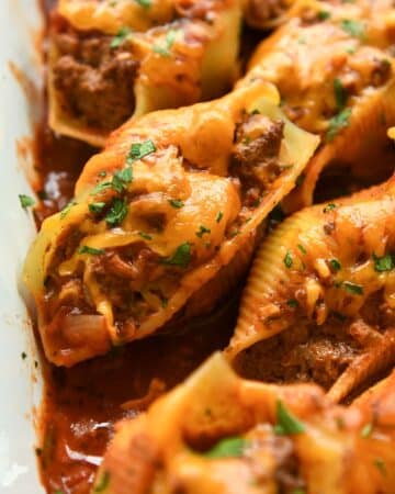 Up close of a stuffed shell sprinkled with chopped cilantro surrounded my other shells in a white baking dish.