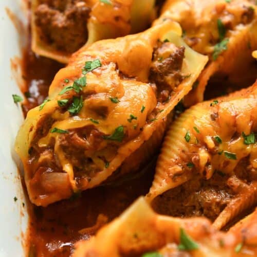 Up close of a stuffed shell sprinkled with chopped cilantro surrounded my other shells in a white baking dish.