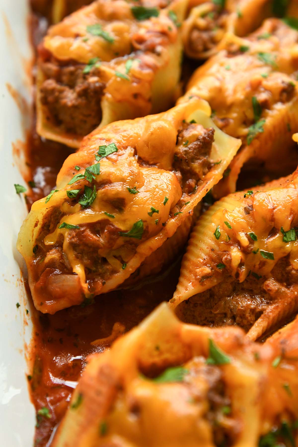 Up close of a stuffed shell sprinkled with chopped cilantro surrounded my other shells in a white baking dish.