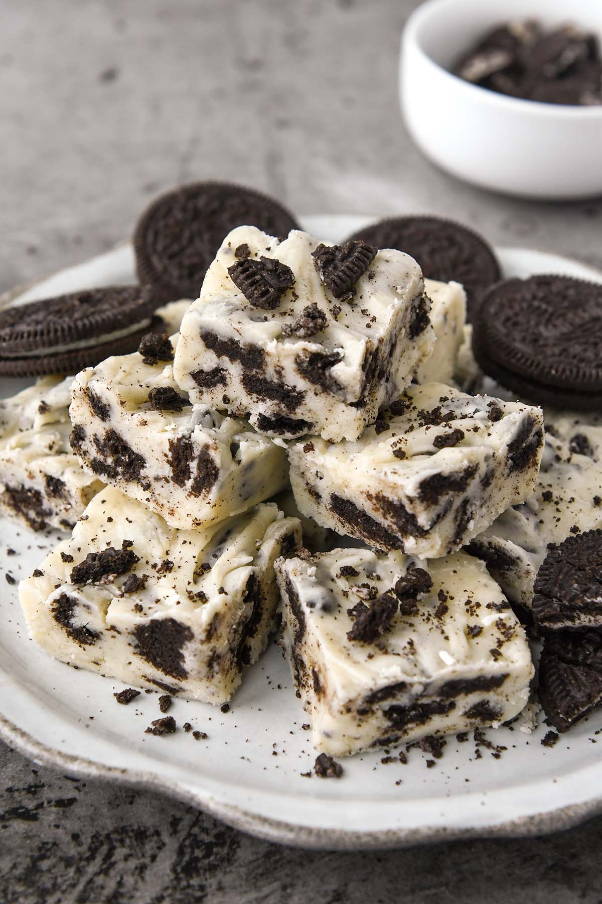 A plate of stacked oreo cookie fudge with some crumbs of Oreo cookies sprinkled on top and whole cookies.