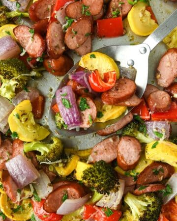 Up close and above view of baked vegetables on a sheet pan with a serving spoon.